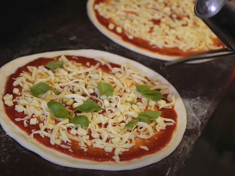 Eine mit Tomatensoße, Käse und Basilikum belegte, ungebackene Pizza.